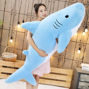 Close-up of a giant blue plush shark pillow held by a person in a cozy room setting