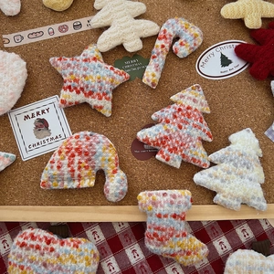 Flat lay of colorful knitted Christmas ornaments including trees and stars on cork