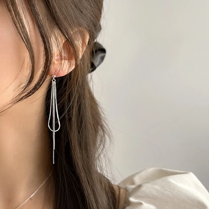 Close-up of minimalist sterling silver snake chain tassel earrings worn by a model