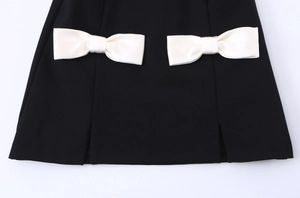 Detail of black sleeveless dress featuring white satin bows and small side slits