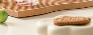Détail de la tasse en verre rose en forme de pétale sur un plateau en bois ondulé