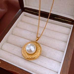 Detailansicht eines vintage Goldanhängers mit Hammerschlag-Optik und Perle in einer Schmuckbox