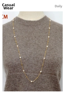 Détail d'un long collier de perles d'eau douce avec billes dorées sur pull marron