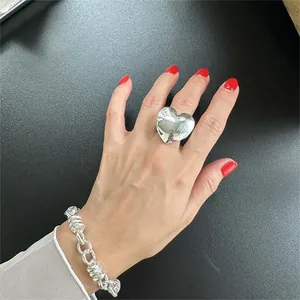 Close-up of polished silver heart ring and chunky link bracelet with red nail polish contrast