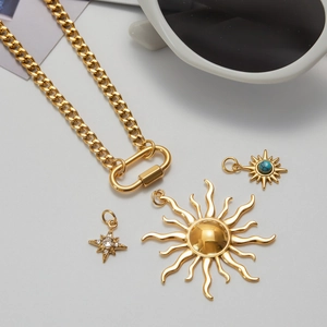Flat lay of gold sun and turquoise star pendants on a carabiner cuban link necklace