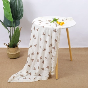 Detailed texture of white cotton gauze baby blanket with brown bear prints and tassels