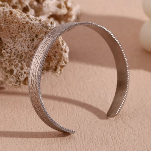 Macro shot of silver hammered texture cuff bracelet on a beige stone pedestal