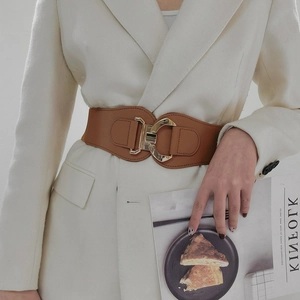 Detail of a wide brown elastic waist belt with a gold geometric metal buckle on a white blazer