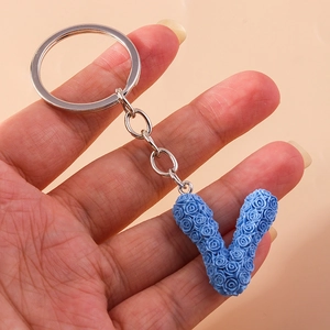 Detail of royal blue letter V keychain with intricate rose floral texture and silver clip