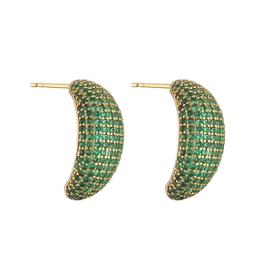 Detailed macro view of gold-plated C-shaped earrings with emerald green zircon pavé stones
