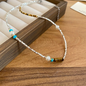 Detail of silver beads with tiger eye and pearls on a wooden jewelry display tray