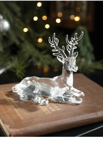 Macro detail of clear acrylic reindeer figurine resting on a vintage book with bokeh lights