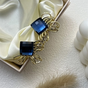 Elegant gold drop earrings with deep blue square crystals on beige silk background