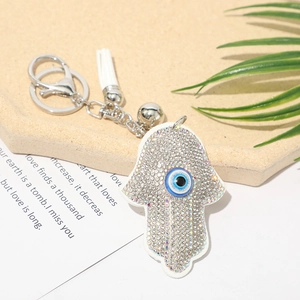 Macro shot of silver Hamsa Hand keychain with blue Evil Eye, rhinestones and white tassel