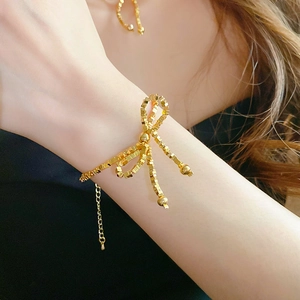 Détail d'un bracelet doré avec nœud papillon et perles cubiques sur le poignet