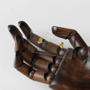 Close-up of golden honeycomb stud earrings with tiny zircon accent on wooden hand model