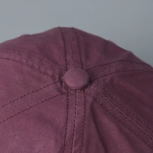 Close-up detail of top button and stitching on burgundy washed cotton baseball cap