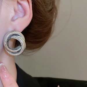Macro shot of silver textured multi-layered knotted earrings on model's ear