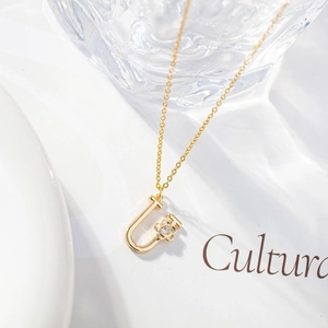 Macro shot of gold letter U pendant featuring a delicate zircon flower on a fine chain