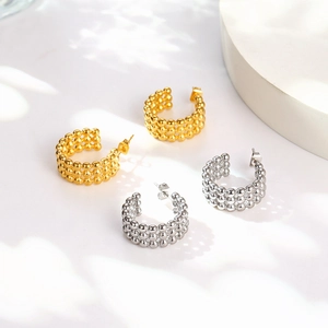 Close-up of geometric C-shaped beaded stud earrings in polished gold and silver steel