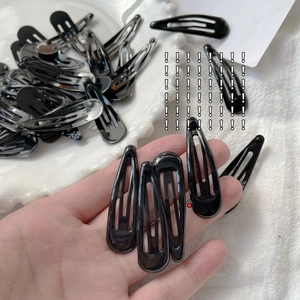 Close-up of classic black teardrop metal BB hair clips on a white ceramic plate