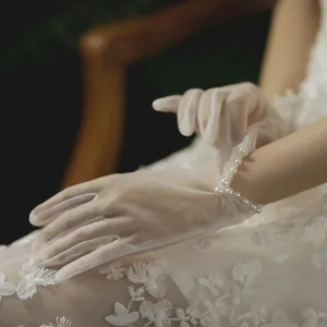 Detail of white sheer tulle bridal gloves with elegant pearl wrist accents and lace trim