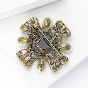 Vintage gold Baroque brooch with white pearls and black gemstone on a white background