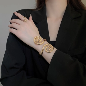 Detailed view of polished golden spiral bracelet and ring set on black background