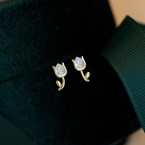 Macro view of gold tulip earrings with clear drop-shaped zircon crystals on dark velvet