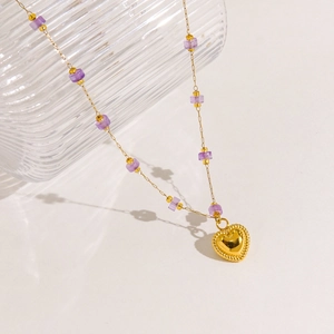 Detailed macro view of a gold heart pendant with purple bead accents on a fine link chain