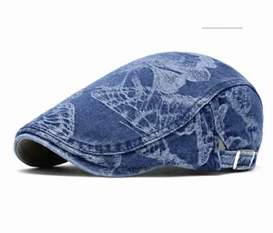 Detail of blue denim newsboy cap featuring butterfly print and metal side buckle