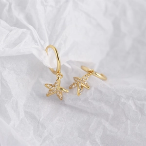 Macro detail of gold starfish earrings with sparkling white zircons on white paper