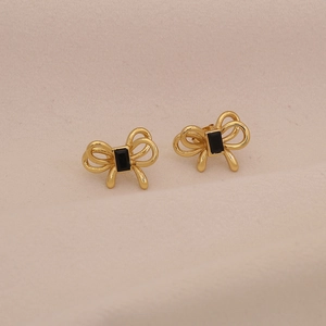 Détail de boucles d'oreilles nœud doré avec une pierre noire carrée au centre