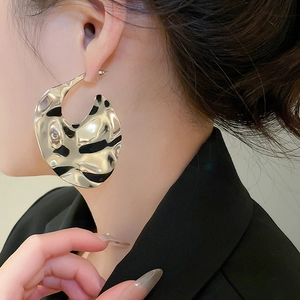 Macro detail of large irregular textured silver metal earrings worn by a model