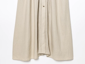 Detail of beige linen dress featuring vertical pleats and a vintage metal button accent