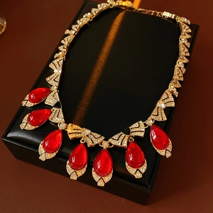 Detailed close-up of golden vintage necklace with red teardrop gem and shiny rhinestones