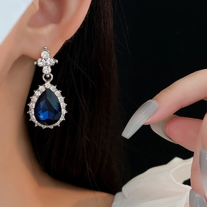 Close-up of model wearing silver teardrop earrings with large faceted blue stone and halo