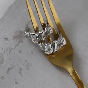 Minimalist silver crinkled foil earrings hanging on a metal fork over stone surface