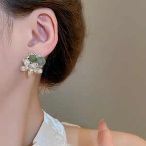 Detailed view of floral pearl and green agate studs worn by a female model