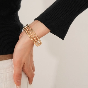 Dettaglio di un bracciale rigido a tre strati di perline dorate sul polso di una modella