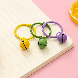 Three colorful resin bell keychains with metal rings on a notebook for DIY bag decor