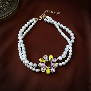 Détail d'un collier de perles double rang avec pendentif fleur en cristal coloré