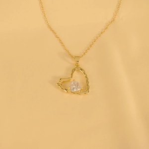 Golden hollow heart pendant necklace with clear sparkling gemstone on yellow fabric