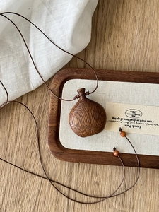 Detail of a minimalist wood water drop pendant with natural texture on a brown wax cord