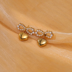 Nahaufnahme goldener Herzohrringe mit Perlenbogen-Detail auf weichem Pfirsichseidenstoff
