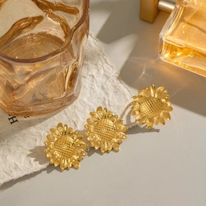 Three-piece gold sunflower stud earrings set on a beige textured background