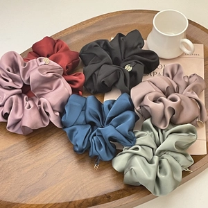 Detail of colorful satin scrunchies with gold charms in a wooden tray home setting