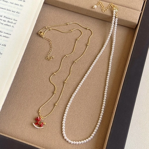 Detail of 18K gold plated horse pendant necklace and pearl strand on beige jewelry tray