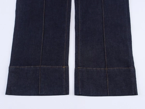 Dettaglio dei pantaloni in denim svasati con cuciture arancioni a contrasto e piega centrale