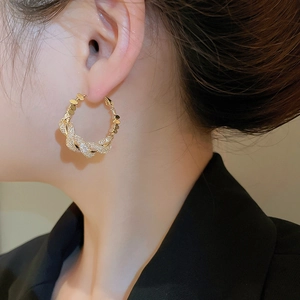 Detail of twisted gold hoop earrings with zircon stones worn by a model for a luxury look